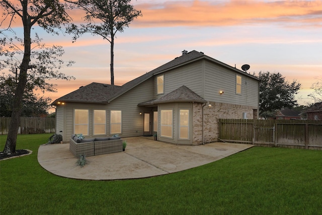 back house at dusk with a patio area, an outdoor living space, and a lawn