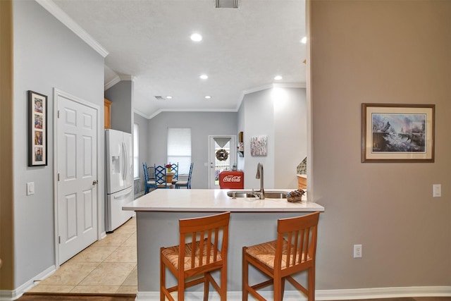 kitchen featuring kitchen peninsula, light tile patterned floors, white fridge with ice dispenser, a kitchen breakfast bar, and sink