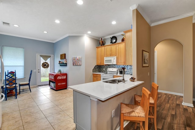 kitchen featuring white appliances, kitchen peninsula, ornamental molding, a kitchen bar, and sink