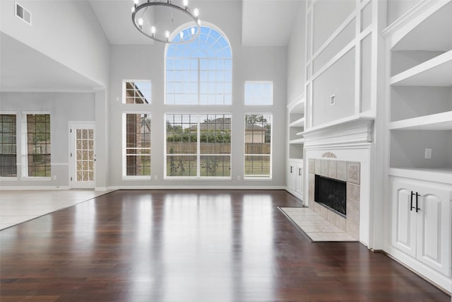 unfurnished living room featuring dark wood-type flooring, an inviting chandelier, a tile fireplace, and built in shelves