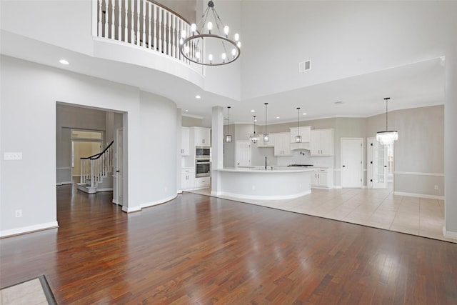 unfurnished living room featuring a towering ceiling, hardwood / wood-style flooring, and an inviting chandelier