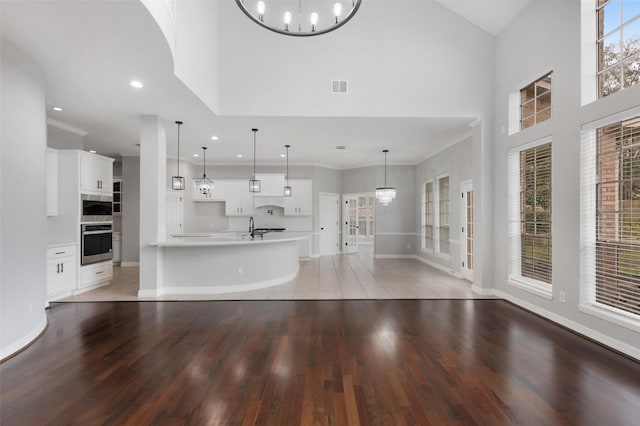 unfurnished living room featuring a high ceiling, a notable chandelier, hardwood / wood-style floors, ornamental molding, and sink