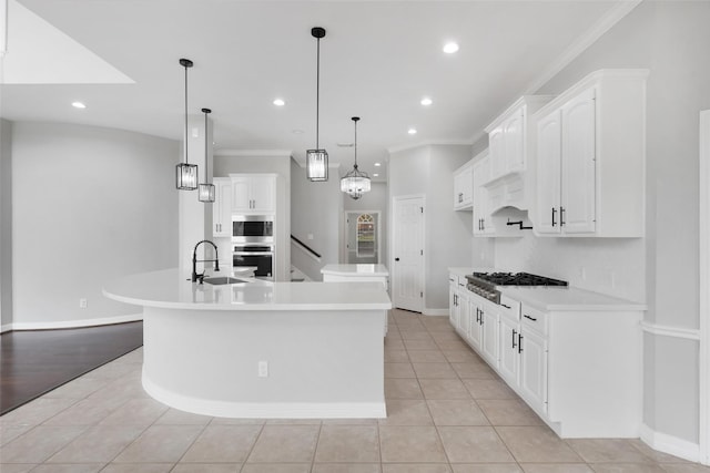 kitchen featuring stainless steel appliances, decorative light fixtures, white cabinetry, and a large island with sink