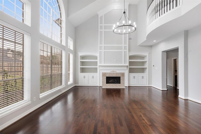 unfurnished living room with dark hardwood / wood-style floors, a high ceiling, a tile fireplace, an inviting chandelier, and built in features