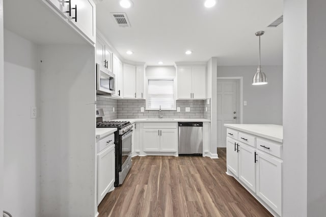 kitchen with appliances with stainless steel finishes, hanging light fixtures, decorative backsplash, white cabinets, and sink