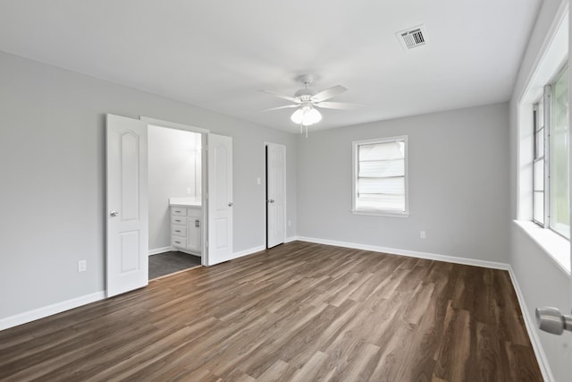 unfurnished bedroom featuring ceiling fan, connected bathroom, multiple windows, and dark hardwood / wood-style floors