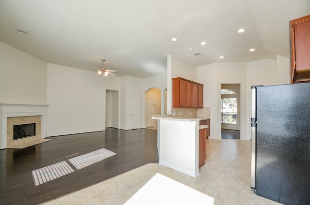 kitchen featuring ceiling fan, a fireplace, kitchen peninsula, decorative backsplash, and stainless steel fridge