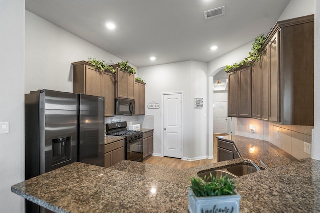 kitchen with kitchen peninsula, dark stone counters, black appliances, and sink