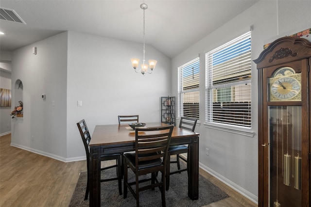 dining area with lofted ceiling, wood-type flooring, and an inviting chandelier