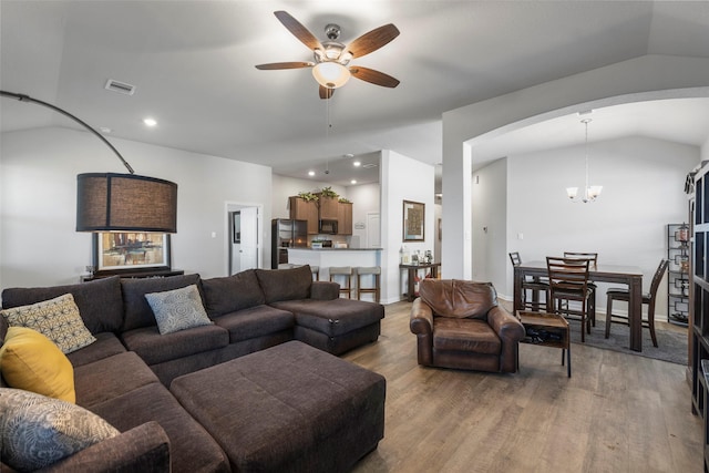 living room featuring light wood-type flooring, lofted ceiling, and ceiling fan with notable chandelier