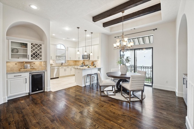 dining area featuring a notable chandelier, a healthy amount of sunlight, beverage cooler, and a raised ceiling