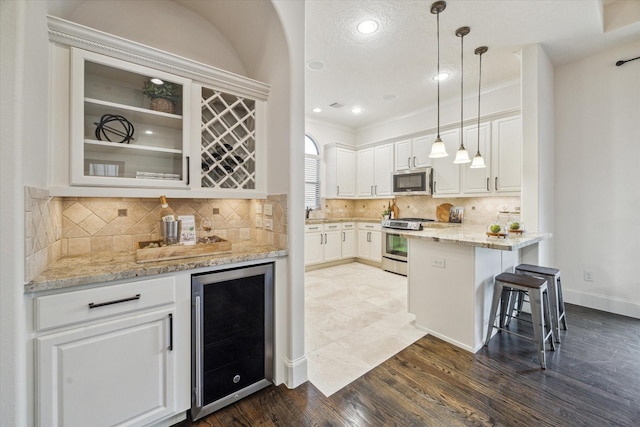 kitchen featuring stainless steel appliances, white cabinets, beverage cooler, and hanging light fixtures