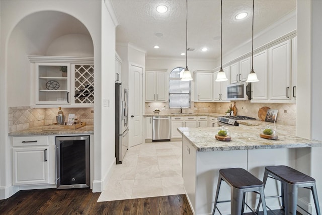 kitchen with beverage cooler, pendant lighting, white cabinetry, and appliances with stainless steel finishes