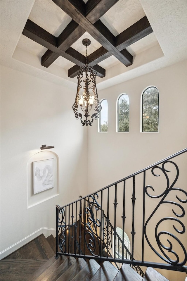 stairs with coffered ceiling, beamed ceiling, a notable chandelier, and parquet floors