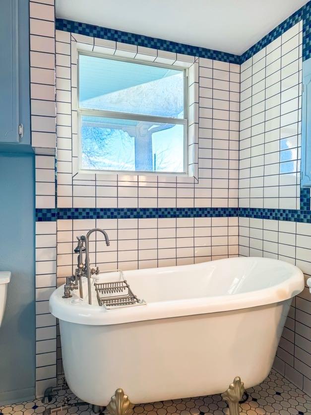 bathroom with tile walls, tile patterned flooring, and a bath