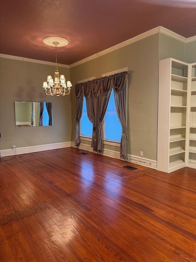 empty room featuring wood-type flooring, a chandelier, and crown molding