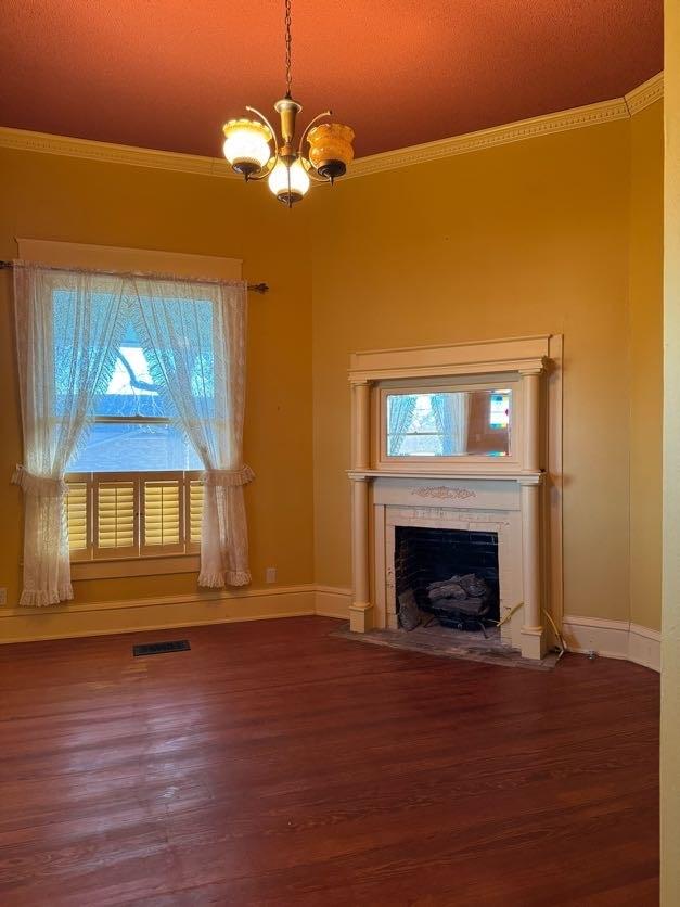 unfurnished living room featuring an inviting chandelier, ornamental molding, and dark hardwood / wood-style flooring