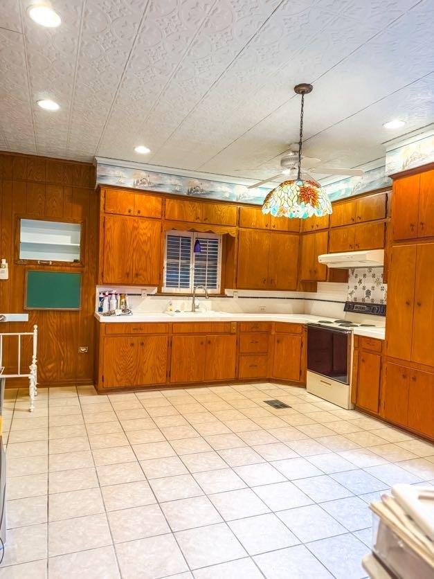 kitchen with white electric stove, light tile patterned floors, wooden walls, sink, and decorative light fixtures