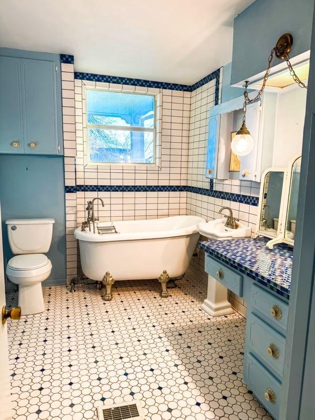 bathroom with toilet, a tub to relax in, tile walls, tile patterned floors, and sink