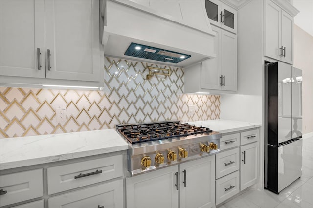 kitchen with fridge, light stone countertops, custom range hood, white cabinets, and stainless steel gas cooktop