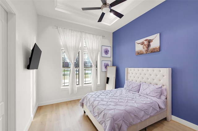 bedroom featuring hardwood / wood-style flooring, ceiling fan, ornamental molding, and a tray ceiling