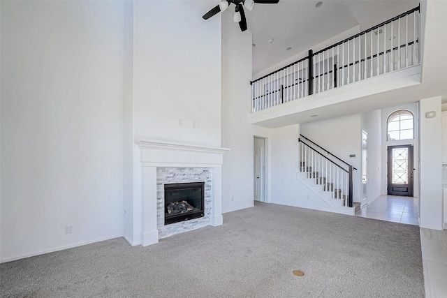 unfurnished living room with a towering ceiling, a tiled fireplace, ceiling fan, and light carpet