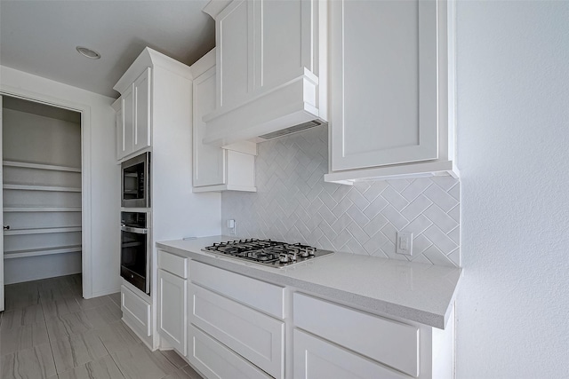 kitchen with white cabinets, stainless steel appliances, backsplash, and premium range hood