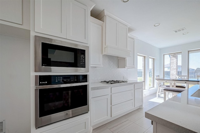 kitchen with white cabinets, oven, tasteful backsplash, and built in microwave