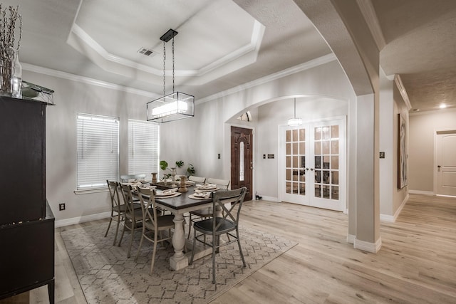 dining area with french doors, ornamental molding, a tray ceiling, and light hardwood / wood-style flooring