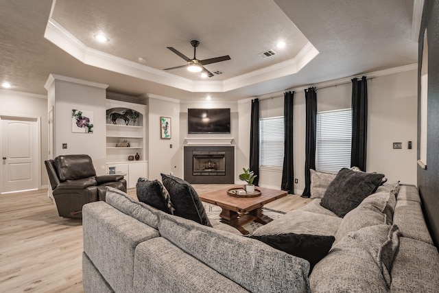 living room with ceiling fan, light wood-type flooring, a tray ceiling, and ornamental molding