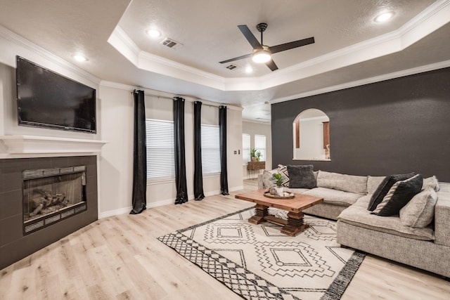 living room with a fireplace, ornamental molding, a tray ceiling, and light hardwood / wood-style flooring