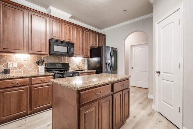 kitchen with black appliances, light hardwood / wood-style floors, crown molding, a kitchen island, and tasteful backsplash