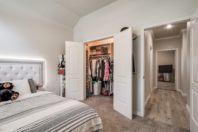 bedroom with a closet, ornamental molding, a spacious closet, light hardwood / wood-style flooring, and lofted ceiling