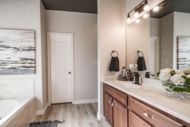 bathroom with wood-type flooring, vanity, and tiled bath