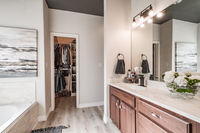 bathroom with wood-type flooring, vanity, and tiled tub