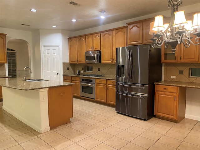 kitchen with stainless steel appliances, an island with sink, light stone countertops, light tile patterned floors, and sink