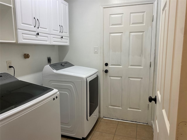 clothes washing area with independent washer and dryer, cabinets, and light tile patterned floors