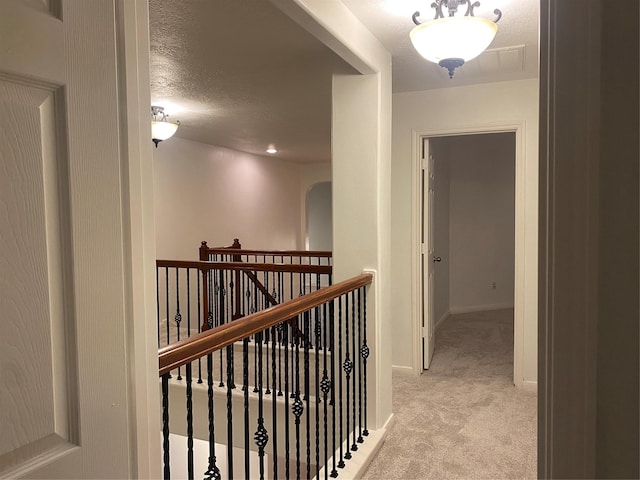 hall with a textured ceiling and light colored carpet