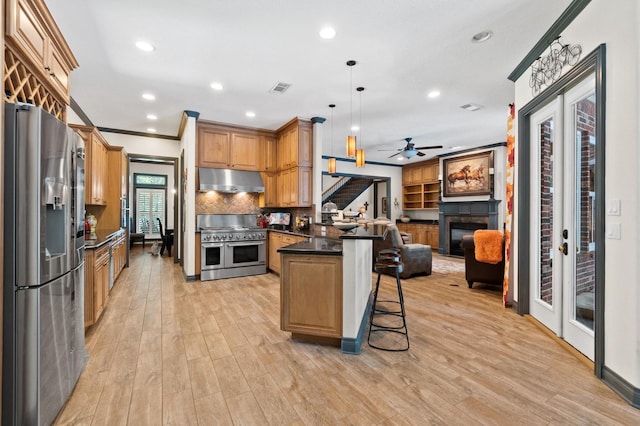 kitchen featuring a breakfast bar area, appliances with stainless steel finishes, crown molding, pendant lighting, and light hardwood / wood-style flooring