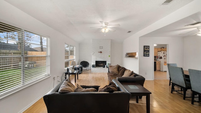 living room with ceiling fan, a fireplace, a textured ceiling, and light hardwood / wood-style flooring