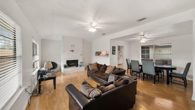 living room featuring ceiling fan, hardwood / wood-style floors, a textured ceiling, and a fireplace