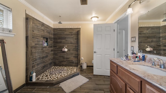 bathroom featuring wood-type flooring, vanity, toilet, tiled shower, and crown molding