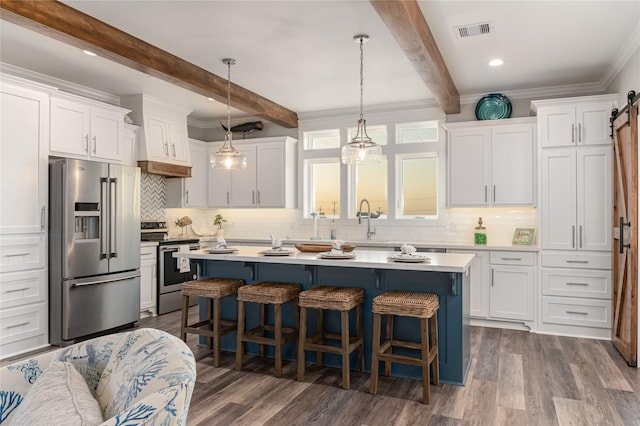 kitchen with appliances with stainless steel finishes, hanging light fixtures, white cabinets, and a barn door