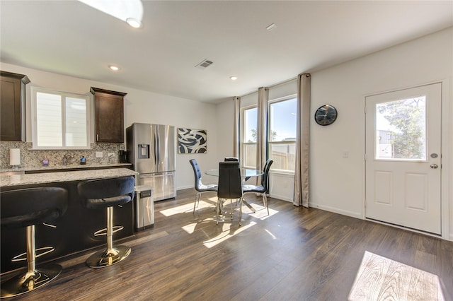 interior space with dark brown cabinets, stainless steel fridge with ice dispenser, a healthy amount of sunlight, and dark hardwood / wood-style floors