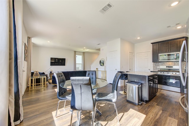 kitchen with stainless steel appliances, a center island, light stone counters, dark brown cabinetry, and dark hardwood / wood-style flooring