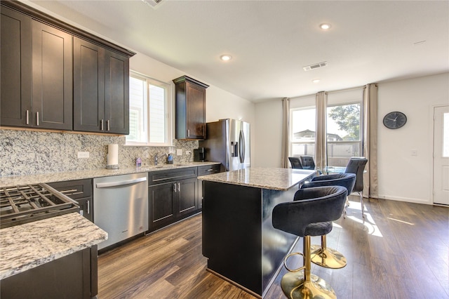 kitchen featuring light stone counters, stainless steel appliances, dark hardwood / wood-style flooring, and a center island