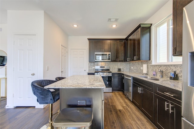 kitchen featuring appliances with stainless steel finishes, a center island, dark hardwood / wood-style floors, dark brown cabinets, and backsplash