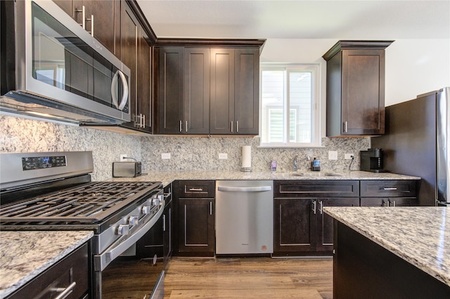 kitchen featuring light stone countertops, decorative backsplash, dark brown cabinetry, appliances with stainless steel finishes, and sink