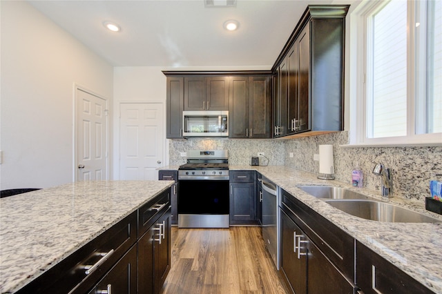 kitchen featuring sink, hardwood / wood-style floors, dark brown cabinets, light stone countertops, and appliances with stainless steel finishes