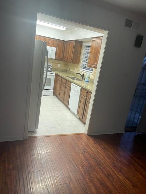 kitchen with sink, white appliances, light hardwood / wood-style flooring, and light stone counters